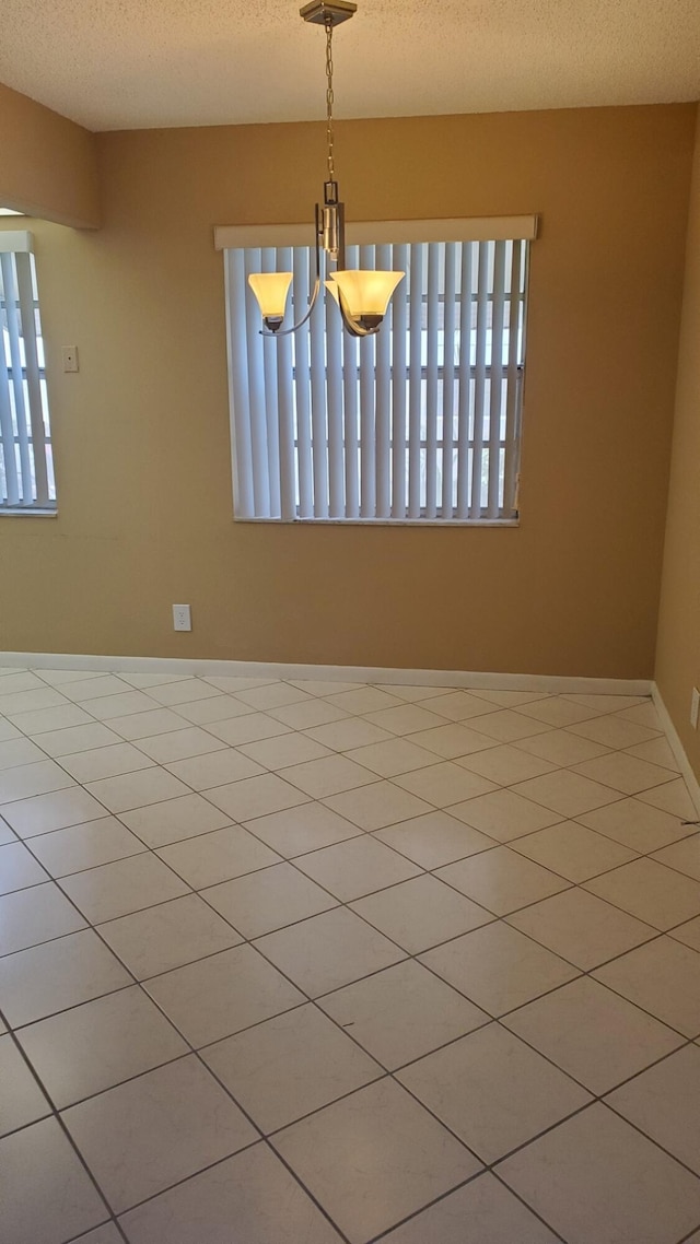 spare room with a textured ceiling, baseboards, a wealth of natural light, and an inviting chandelier