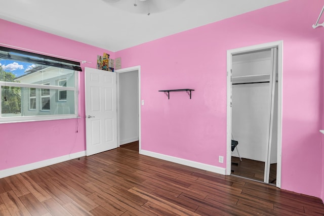 unfurnished bedroom featuring ceiling fan, a closet, baseboards, and dark wood-type flooring