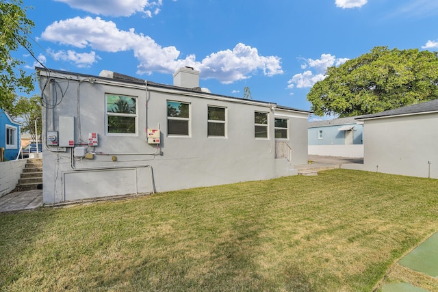 back of property featuring a yard, a chimney, and stucco siding