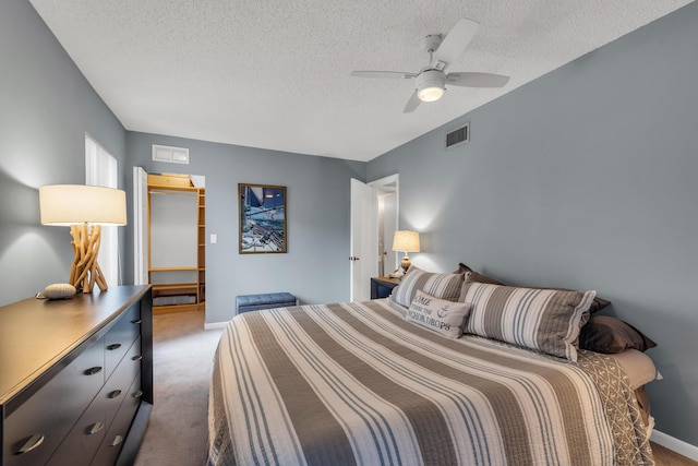 carpeted bedroom featuring a ceiling fan, visible vents, a walk in closet, and a textured ceiling