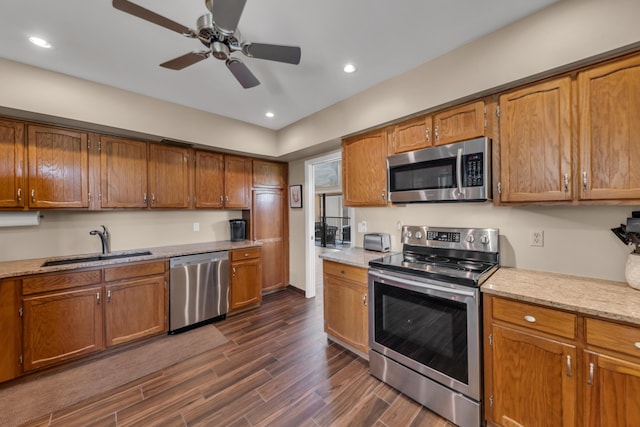 kitchen featuring brown cabinetry, appliances with stainless steel finishes, dark wood-style flooring, and a sink