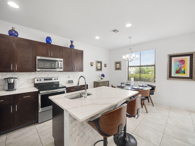 kitchen featuring light tile patterned floors, a center island with sink, appliances with stainless steel finishes, pendant lighting, and a sink