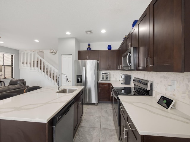 kitchen featuring stainless steel appliances, a sink, tasteful backsplash, dark brown cabinets, and open floor plan