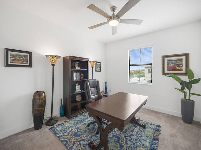 carpeted office space featuring a ceiling fan and baseboards