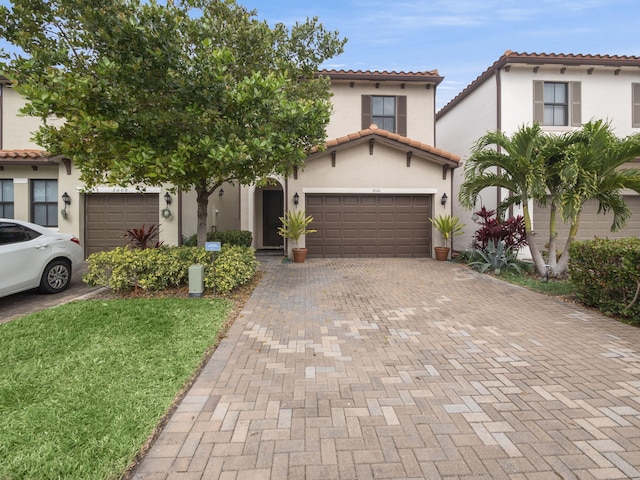 mediterranean / spanish-style house with a garage, decorative driveway, a tile roof, and stucco siding