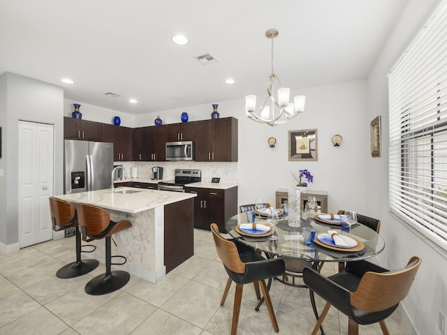 kitchen with stainless steel appliances, a sink, a chandelier, decorative backsplash, and dark brown cabinets