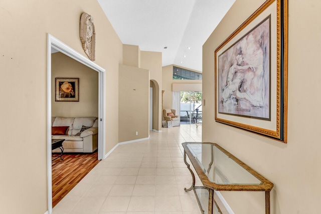 corridor with vaulted ceiling, light tile patterned flooring, arched walkways, and baseboards