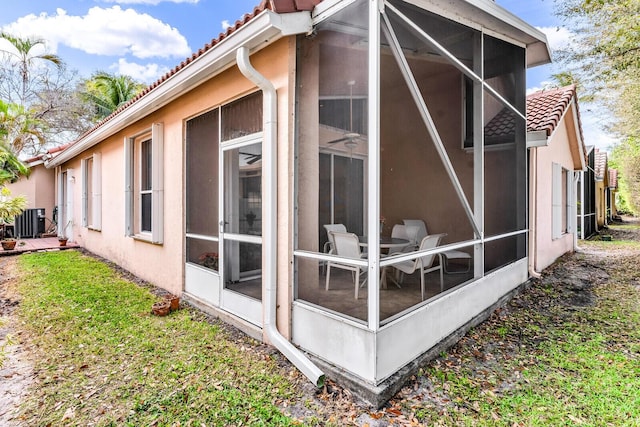 view of home's exterior with a sunroom, stucco siding, cooling unit, and a tiled roof