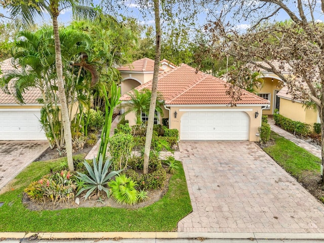 mediterranean / spanish house with decorative driveway, a tile roof, an attached garage, and stucco siding