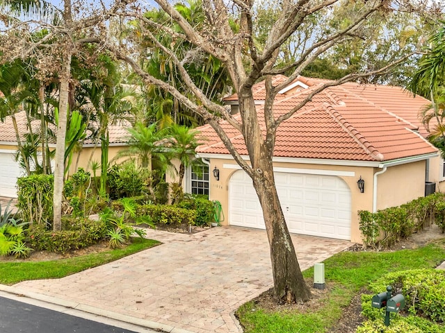 mediterranean / spanish-style house featuring a garage, decorative driveway, a tile roof, and stucco siding