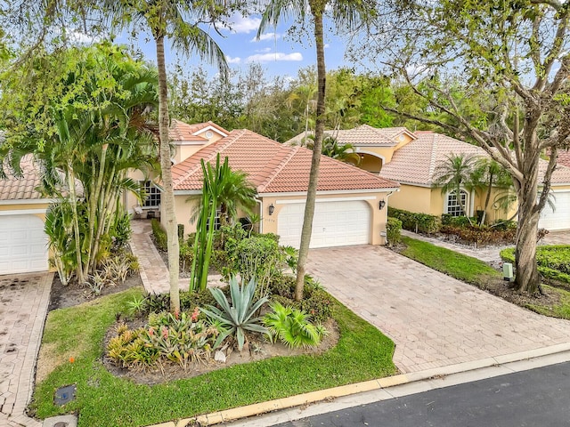 mediterranean / spanish house featuring a garage, a tiled roof, decorative driveway, and stucco siding