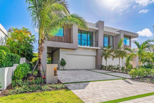 modern home featuring a garage, decorative driveway, fence, and stucco siding