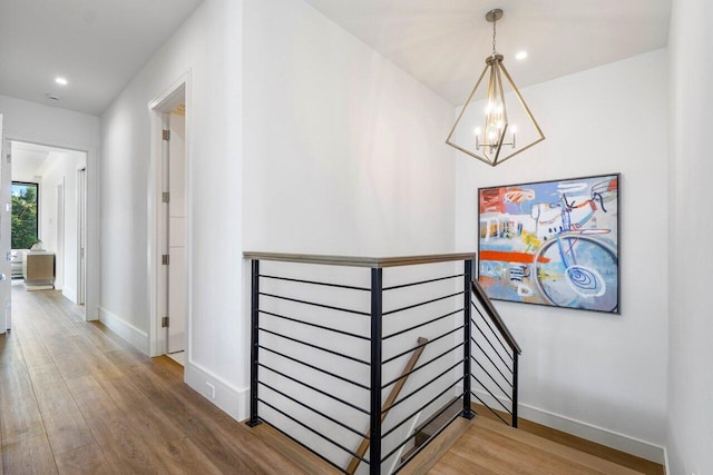 corridor featuring an inviting chandelier, baseboards, wood finished floors, and an upstairs landing