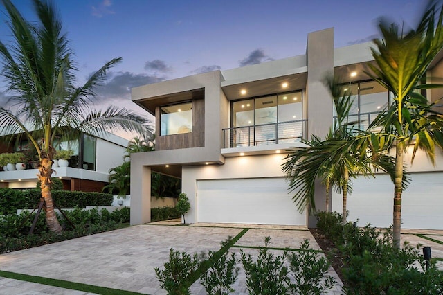 view of front facade featuring an attached garage, decorative driveway, stucco siding, and a balcony