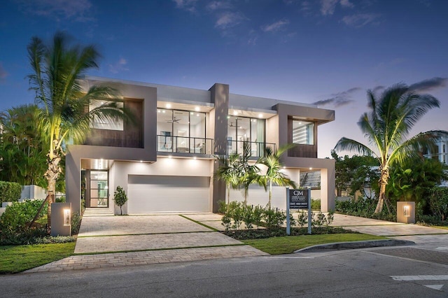 modern home with decorative driveway, an attached garage, a balcony, and stucco siding