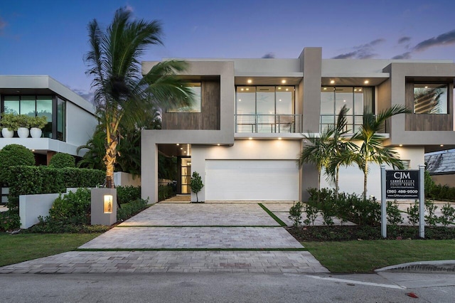 contemporary house with decorative driveway, an attached garage, a balcony, and stucco siding