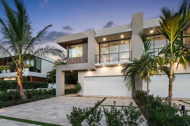 contemporary home featuring driveway, a balcony, an attached garage, and stucco siding