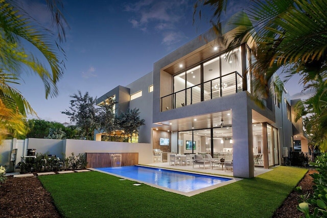 rear view of property with fence, stucco siding, a balcony, a ceiling fan, and a patio