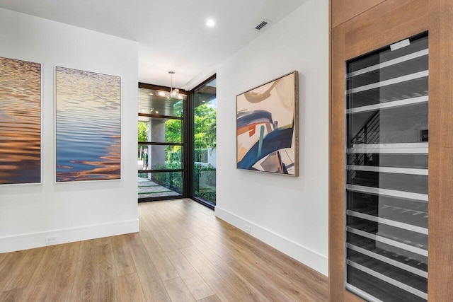 empty room featuring floor to ceiling windows, recessed lighting, wood finished floors, beverage cooler, and baseboards