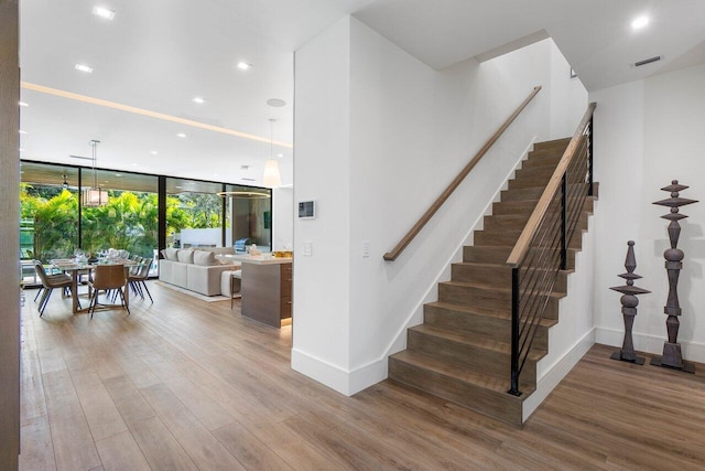 stairway with floor to ceiling windows, recessed lighting, visible vents, wood finished floors, and baseboards