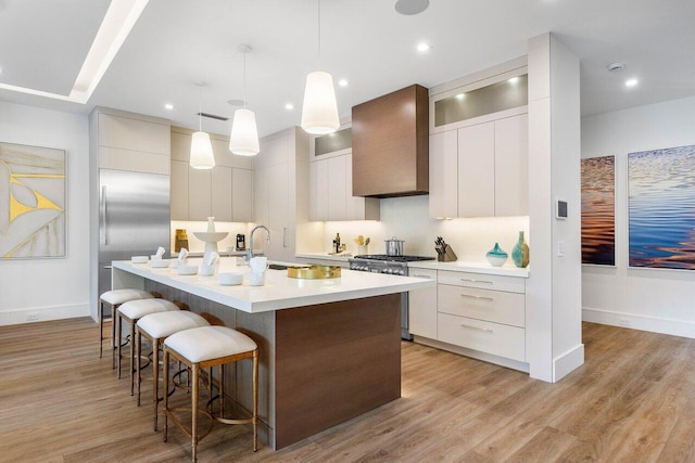 kitchen featuring an island with sink, wall chimney exhaust hood, modern cabinets, and high end appliances