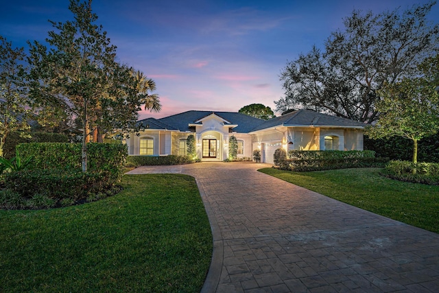 ranch-style home featuring a garage, a yard, decorative driveway, and stucco siding