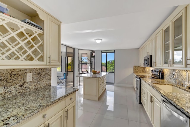 kitchen featuring cream cabinetry, appliances with stainless steel finishes, a sink, and glass insert cabinets