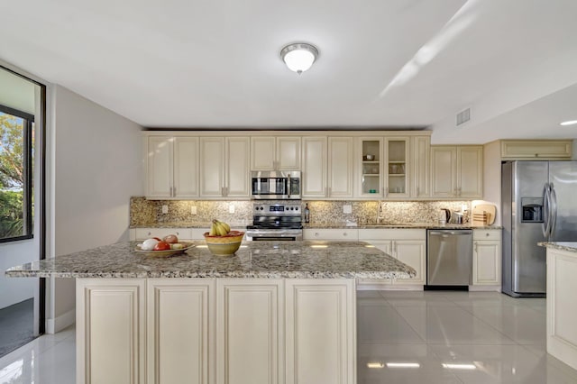 kitchen with stainless steel appliances, a center island, glass insert cabinets, and cream cabinets