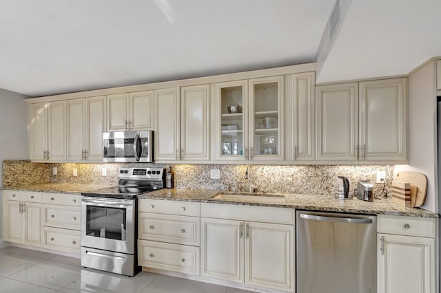 kitchen with appliances with stainless steel finishes, cream cabinets, a sink, and glass insert cabinets