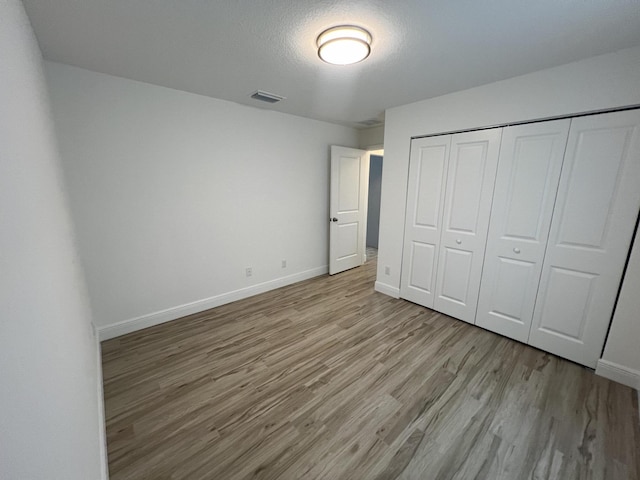 unfurnished bedroom featuring a closet, visible vents, a textured ceiling, light wood-type flooring, and baseboards