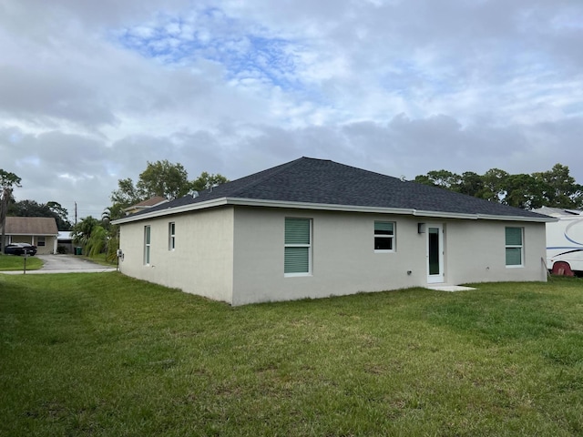 back of property featuring a yard, roof with shingles, and stucco siding