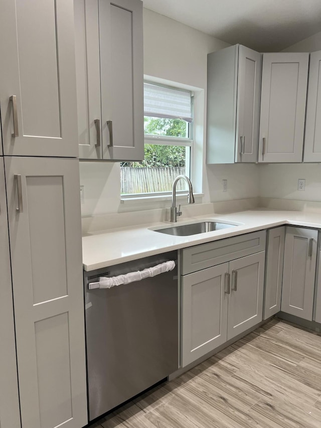 kitchen with dishwasher, light countertops, gray cabinetry, light wood-style floors, and a sink