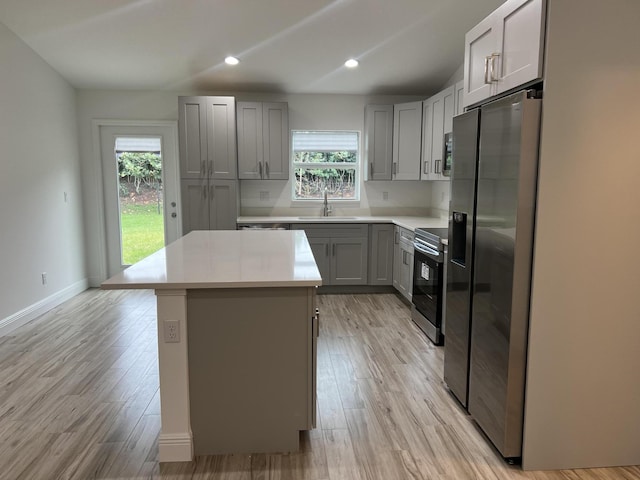 kitchen featuring a sink, light countertops, appliances with stainless steel finishes, gray cabinets, and a center island