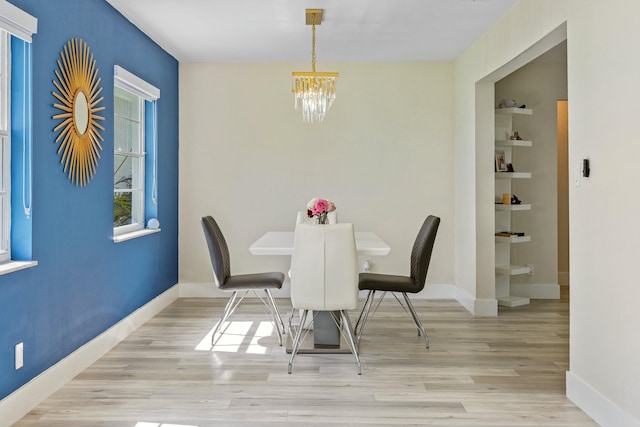 unfurnished dining area with built in shelves, light wood-type flooring, baseboards, and an inviting chandelier