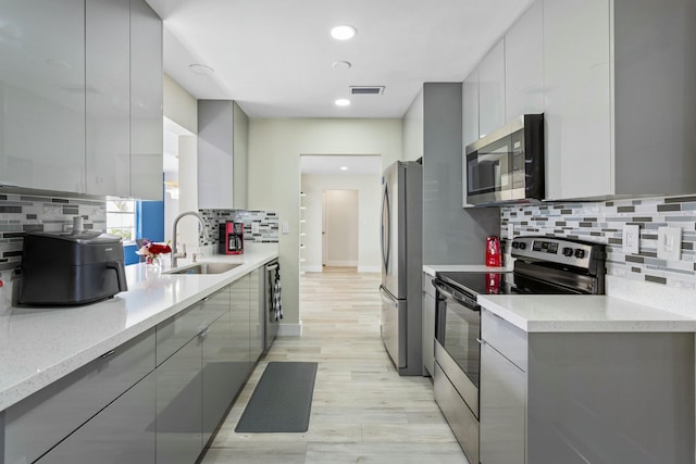 kitchen featuring appliances with stainless steel finishes, a sink, gray cabinetry, and modern cabinets