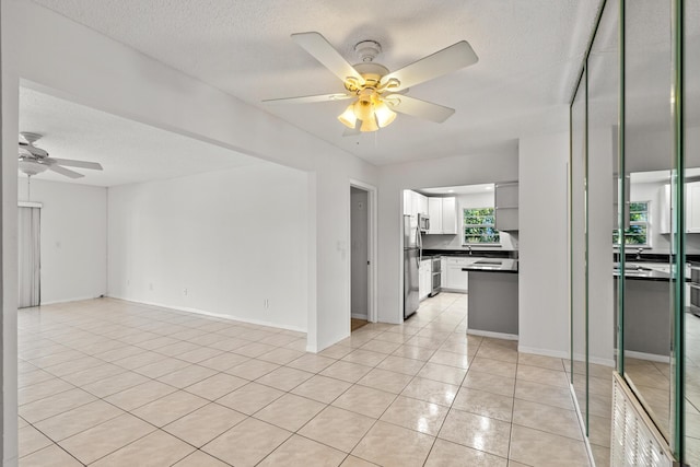 unfurnished living room featuring light tile patterned flooring, baseboards, a textured ceiling, and ceiling fan