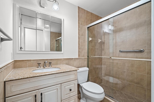 full bath with a shower stall, toilet, vanity, wainscoting, and tile walls