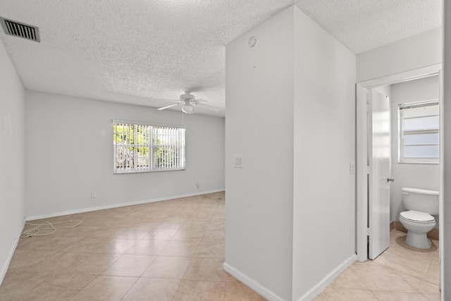 unfurnished room featuring visible vents, baseboards, ceiling fan, light tile patterned floors, and a textured ceiling