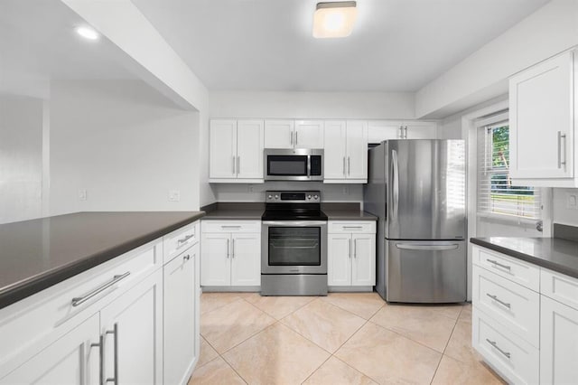 kitchen featuring stainless steel appliances, dark countertops, light tile patterned flooring, and white cabinets