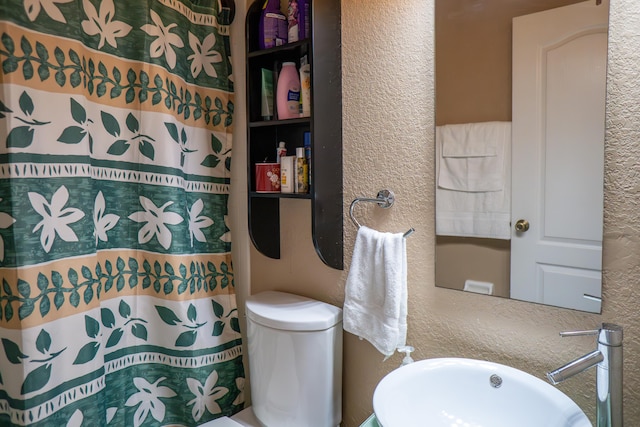 bathroom with toilet, a shower with curtain, a sink, and a textured wall