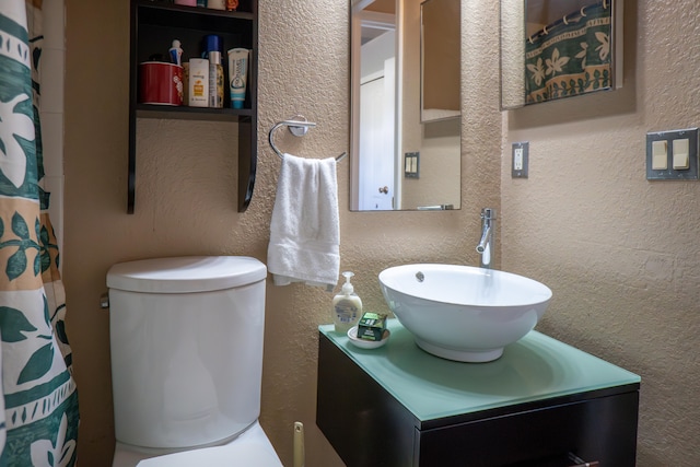 full bath featuring toilet, vanity, and a textured wall
