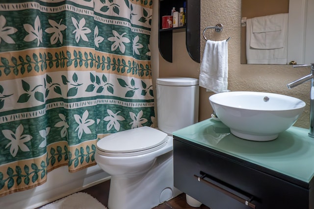 full bathroom featuring shower / bathtub combination with curtain, a textured wall, vanity, and toilet