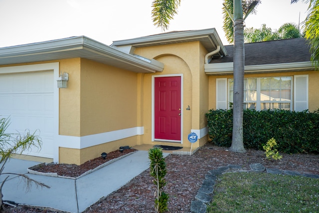 entrance to property with a garage, roof with shingles, and stucco siding
