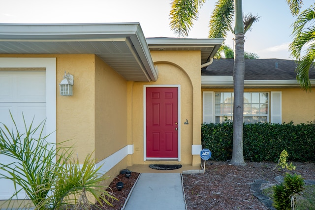 entrance to property featuring a garage, a shingled roof, and stucco siding