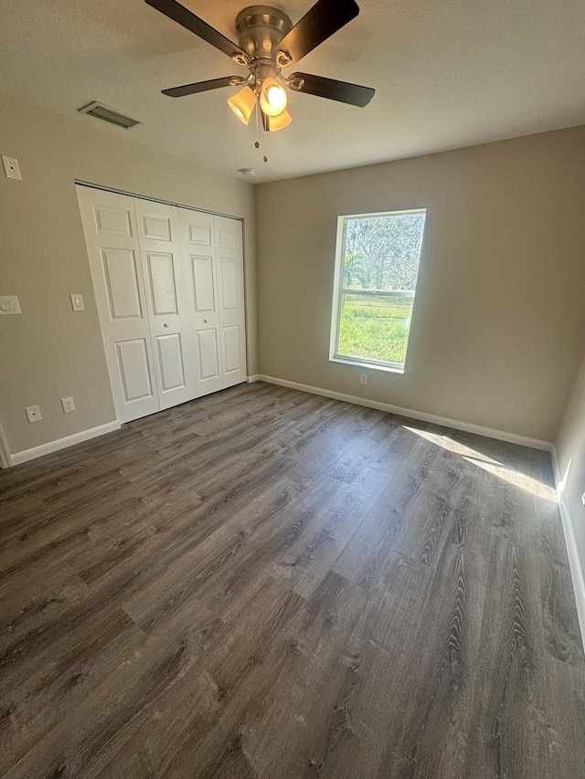 unfurnished bedroom featuring dark wood finished floors, a closet, visible vents, a ceiling fan, and baseboards