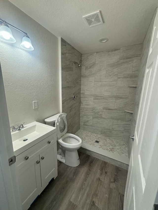 bathroom with a textured wall, wood finished floors, vanity, visible vents, and a shower stall