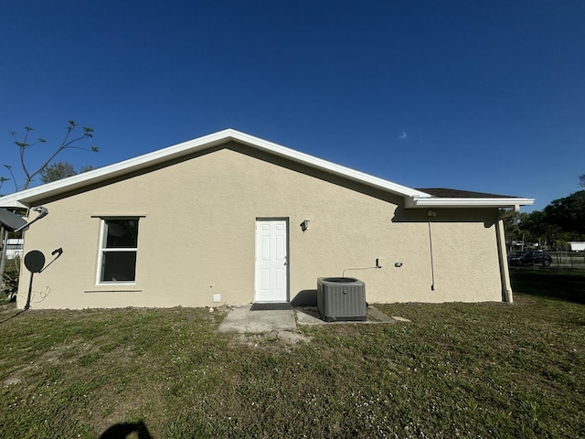 rear view of property with a yard, central AC, and stucco siding