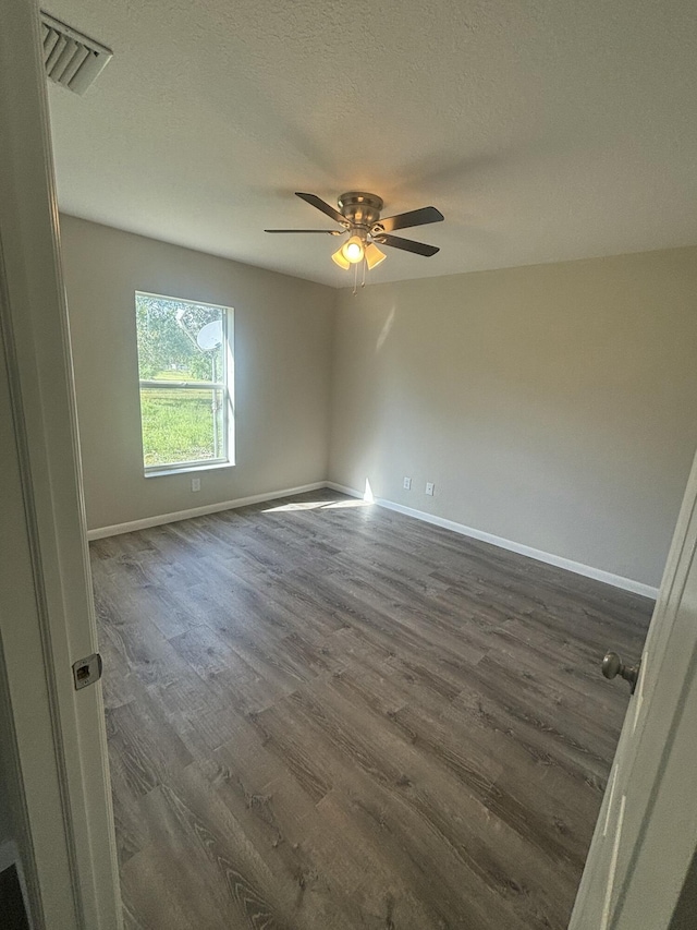 spare room featuring visible vents, dark wood-type flooring, ceiling fan, a textured ceiling, and baseboards