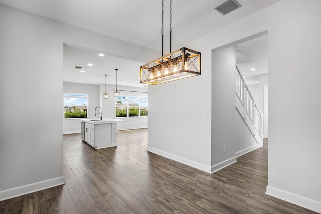 unfurnished dining area featuring dark wood finished floors, a sink, baseboards, and stairs