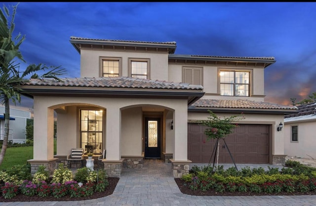 mediterranean / spanish-style house featuring covered porch, stone siding, and stucco siding